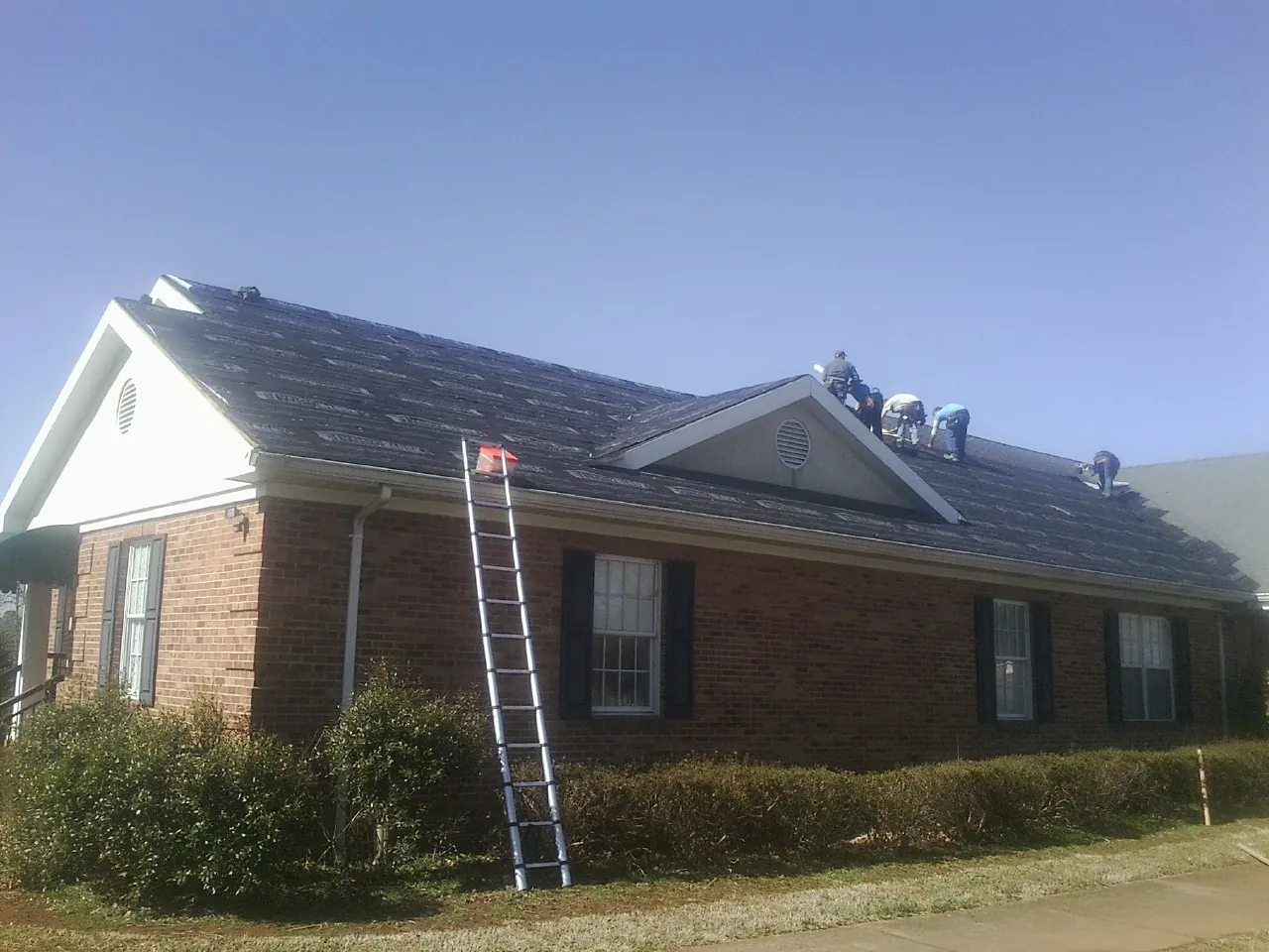 Crew tearing shingles off a brick ranch roof with a ladder set — Emergency Roof Repair work by our crew in Adger
