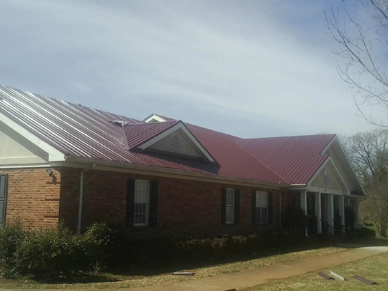 Red metal roof with gabled entries on a long brick building, from a Hail Damage Roof Repair job in Adger