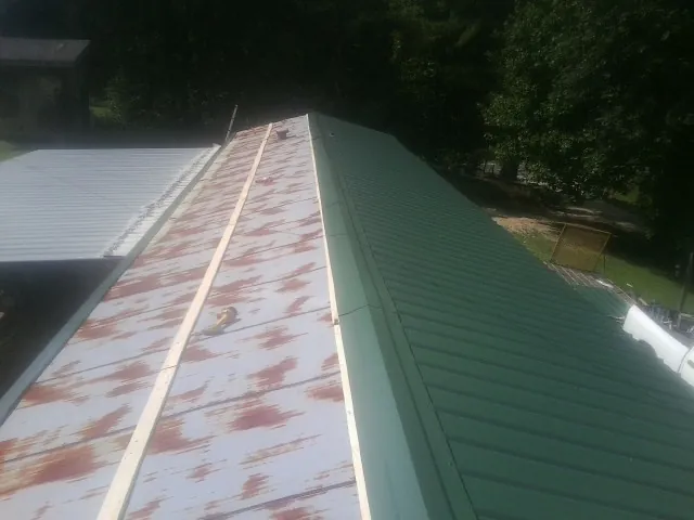 Old rusted panels beside newly installed green metal roofing — Wind Damage Roof Repair by Roofing Brothers in Adger