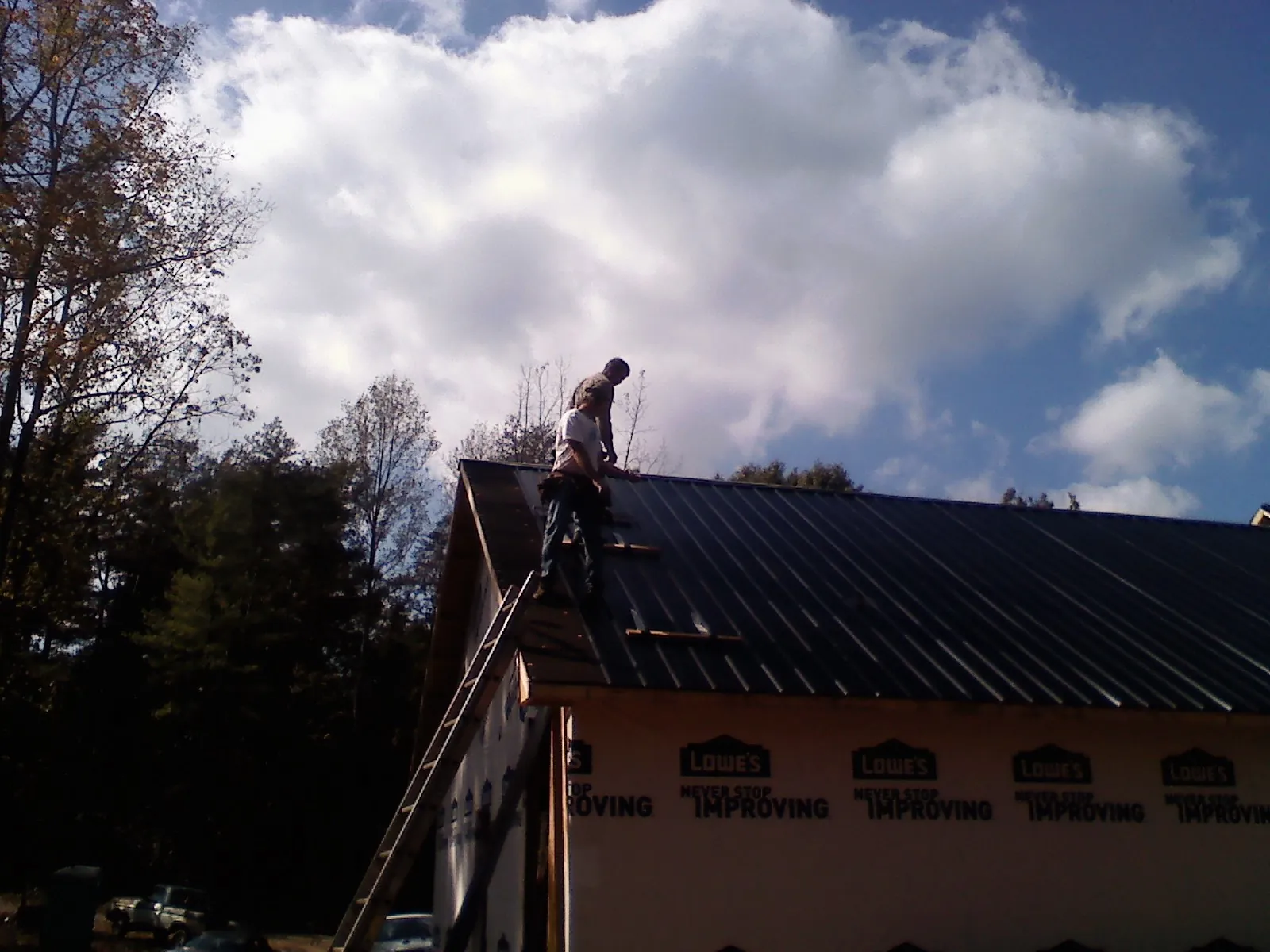 Roofer fastening dark metal panels high against a cloudy sky, from a Roof Inspection job in Adger