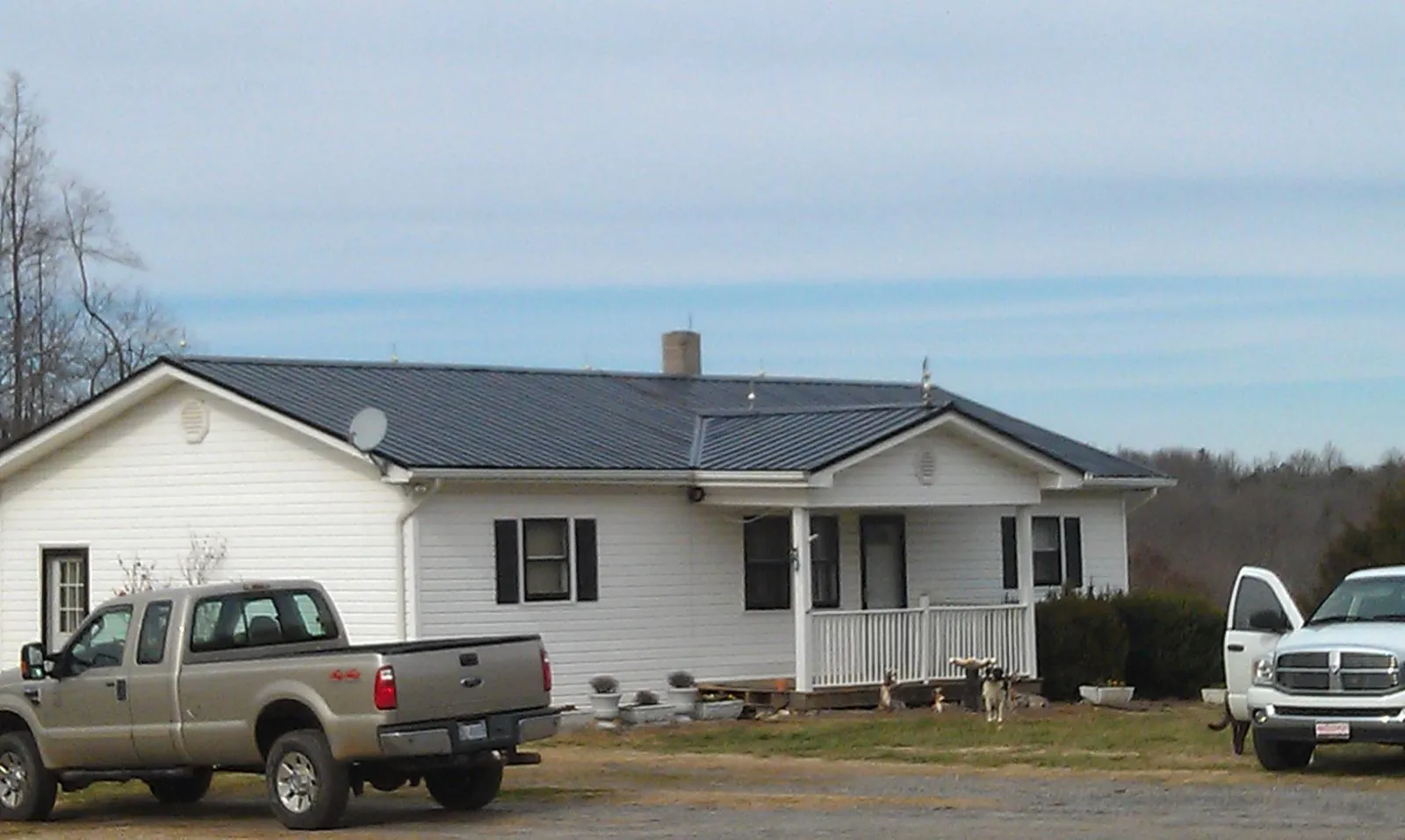 Finished dark metal roof on a white ranch home with work trucks parked in Adger